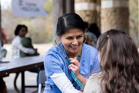 Volunteer nurse smiles while checking young girl at park clinic - stock photo