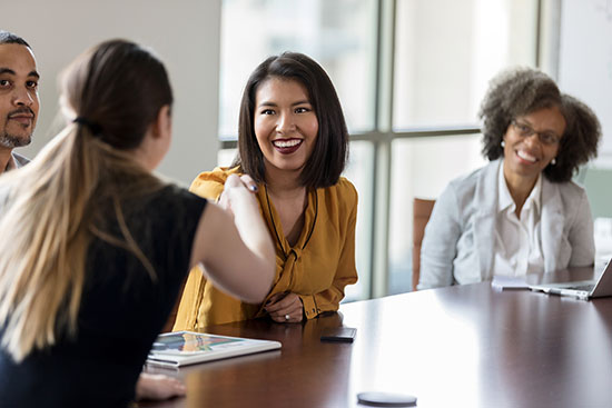 Businesspeople greet one another - stock photo Cheerful mid adult businesswoman greets a colleague with a handshake before a meeting.