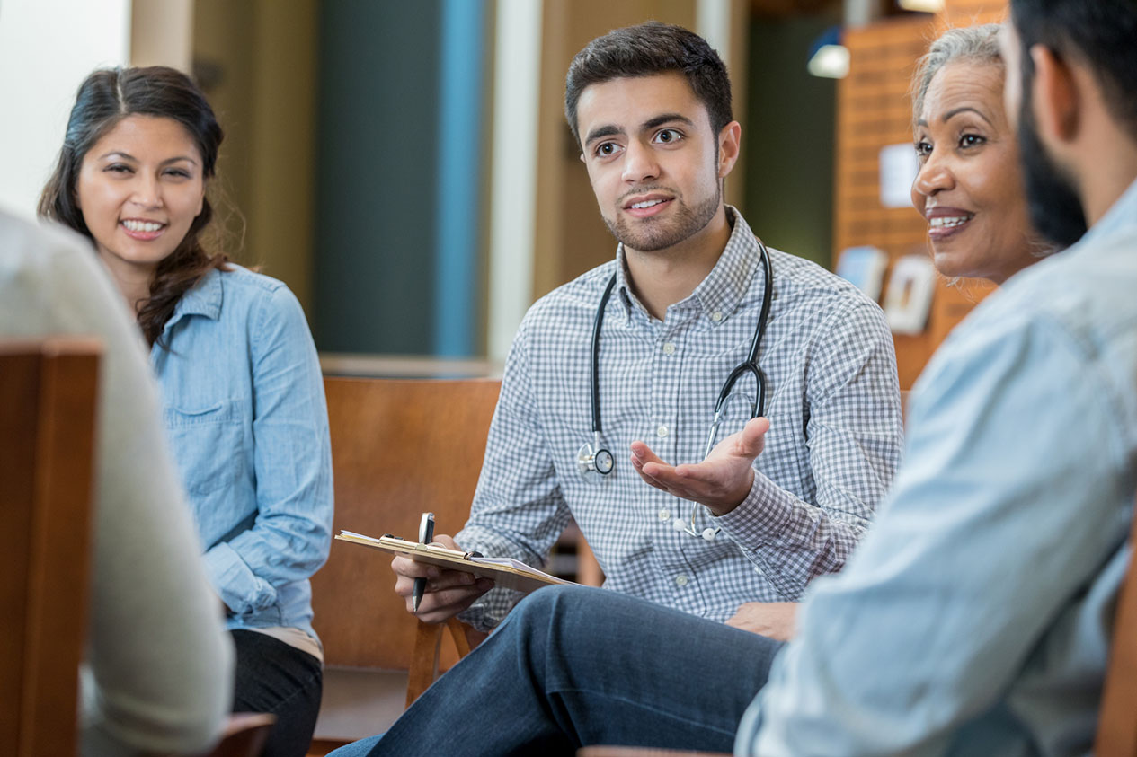 Young physician and colleagues discuss ideas during a meeting. They are are smiling while talking with one another.