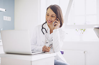 Doctor is on the phone and looking at a laptop computer.