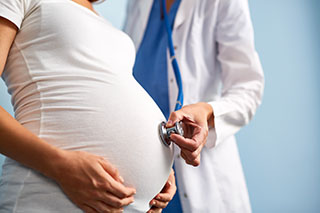 Doctor listening breath of baby in pregnant female abdomen.