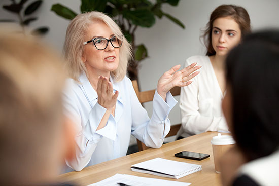 Aged businesswoman, teacher or business coach speaking to young people - stock photo