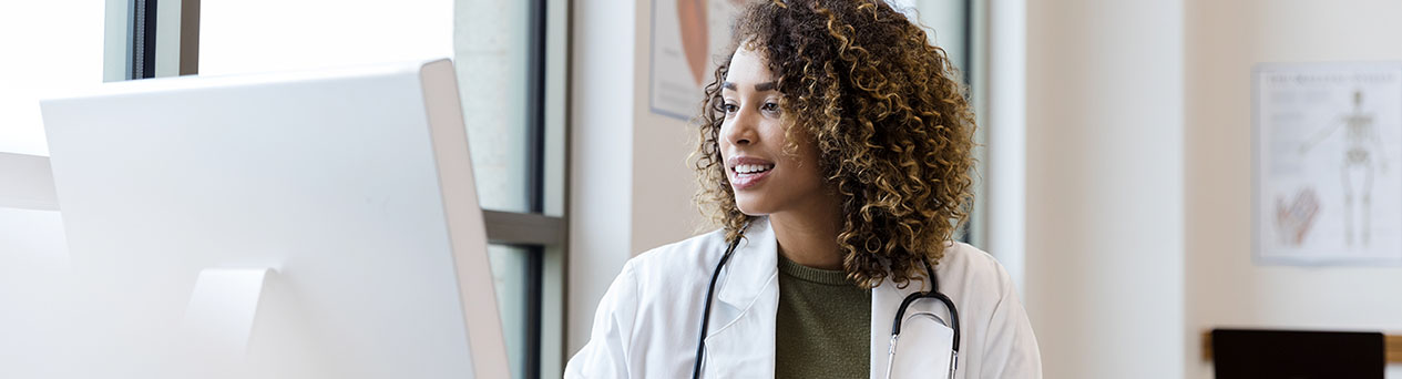 Mid adult female doctor reviews patient records on desktop PC - stock photo